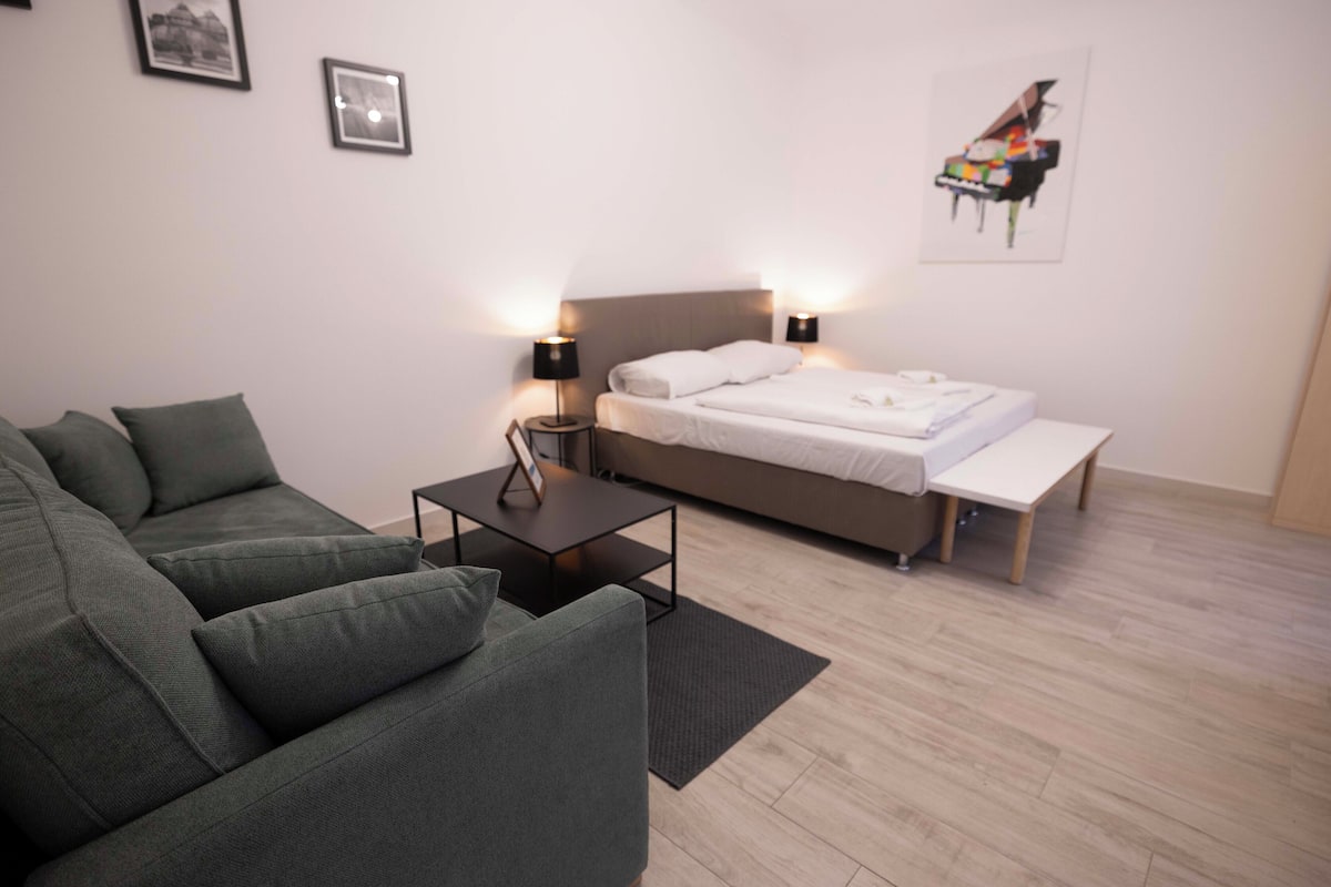 A modern bedroom with a bed, bedside tables, a sofa, and a wooden floor.