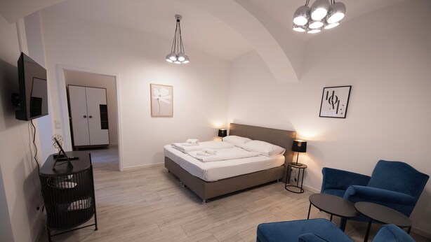 Une chambre moderne avec un lit, des tables de chevet, une télévision et un fauteuil bleu.