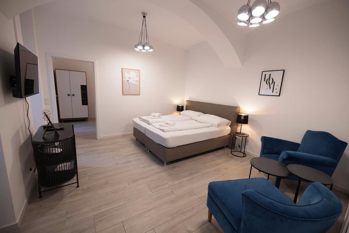 A modern bedroom with a bed, bedside tables, a TV, and a blue armchair.