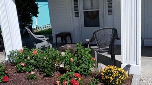 A covered porch with outdoor seating, a small garden with flowers, and a white building with a blue door. - Just  a 2 minute walk to the Atlantic Ocean!
 (Surf City)