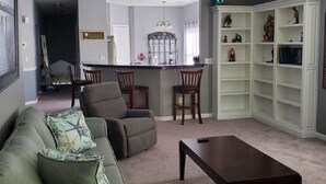 A living room with a sofa, chairs, a coffee table, a kitchen area with a counter and cabinets, and a bookshelf. - 3 Bedroom Condo in Myrtle Beach (Myrtle Beach)