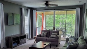 A living room with a sofa, coffee table, TV, and a balcony with a table and chairs. - 3 Bedroom Condo in Myrtle Beach (Myrtle Beach)
