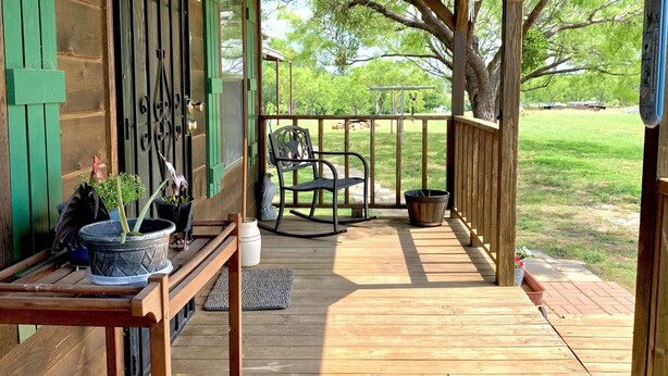 Una terraza de madera con porche cubierto, mobiliario exterior y plantas en macetas.