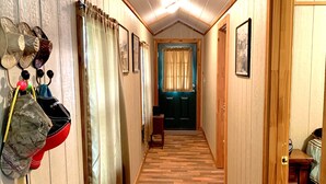 Un pasillo estrecho con suelo de madera, techo con lámpara y una puerta al final que da a otra habitación.