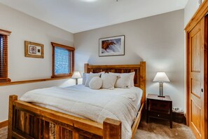 Une chambre à coucher avec un lit en bois, deux tables de chevet avec des lampes, un tableau encadré au mur et une porte.