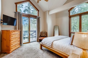 Une chambre à coucher avec un lit, une commode en bois, une télévision et de grandes fenêtres.
