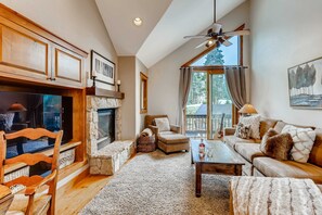 A cozy living room with a fireplace, wooden furniture, and a large window with curtains. - Snow Chateau - Ski In/Out|Walk to Main St|Hot Tub (Breckenridge)