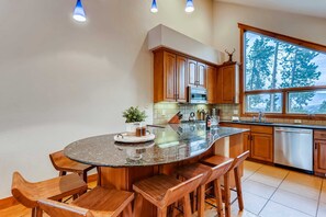 A kitchen with wooden cabinets, a large island with bar stools, a microwave, and a dishwasher. - Snow Chateau - Ski In/Out|Walk to Main St|Hot Tub (Breckenridge)