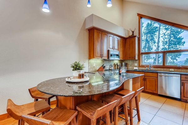 A kitchen with wooden cabinets, a large island with bar stools, a microwave, and a dishwasher. - Snow Chateau - Ski In/Out|Walk to Main St|Hot Tub (Breckenridge)