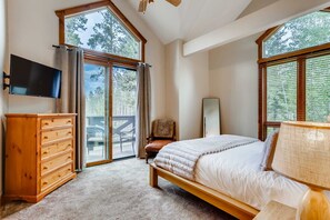 Une chambre à coucher avec un lit, une commode en bois, une télévision et de grandes fenêtres.