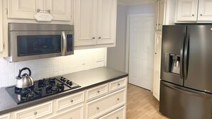 A kitchen with white cabinets, a stainless steel microwave, a gas stove, and a refrigerator.