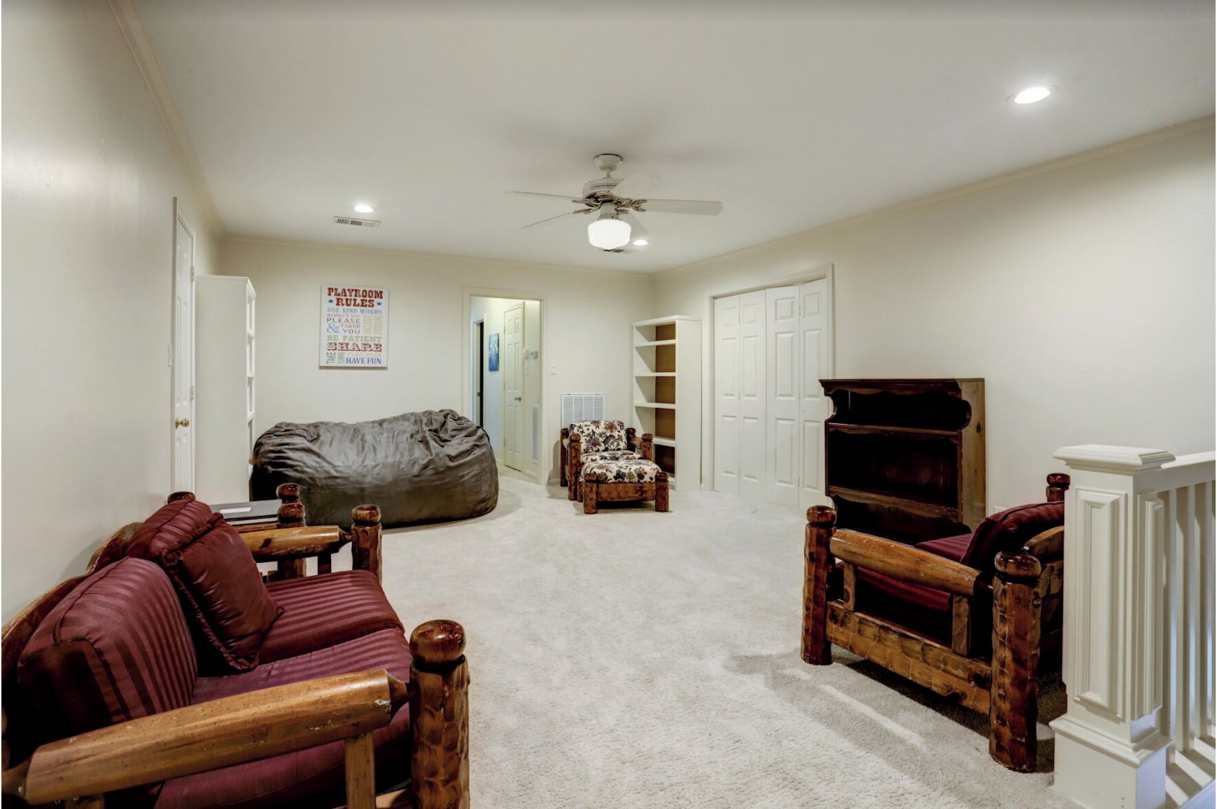 A living room with a large bean bag, a wooden sofa, a patterned armchair, a television, and a ceiling fan.
