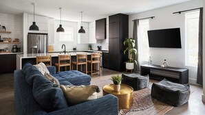 A modern living room with a blue sofa, a coffee table, and a TV. - Stylish 3-Bed Retreat, Rooftop, Parking, Sleeps 10  |  Ensuite Baths, Bunk Room, Gourmet Kitchen, Cozy Living Space, Rooftop Views & Fire Table, Near Downtown, Distilleries & Marathon Village, 24 Hr Hospitality (Nashville)