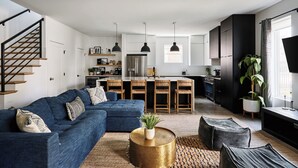 A modern living room with a blue sofa, a coffee table, and a staircase. - Stylish 3-Bed Retreat, Rooftop, Parking, Sleeps 10  |  Ensuite Baths, Bunk Room, Gourmet Kitchen, Cozy Living Space, Rooftop Views & Fire Table, Near Downtown, Distilleries & Marathon Village, 24 Hr Hospitality (Nashville)