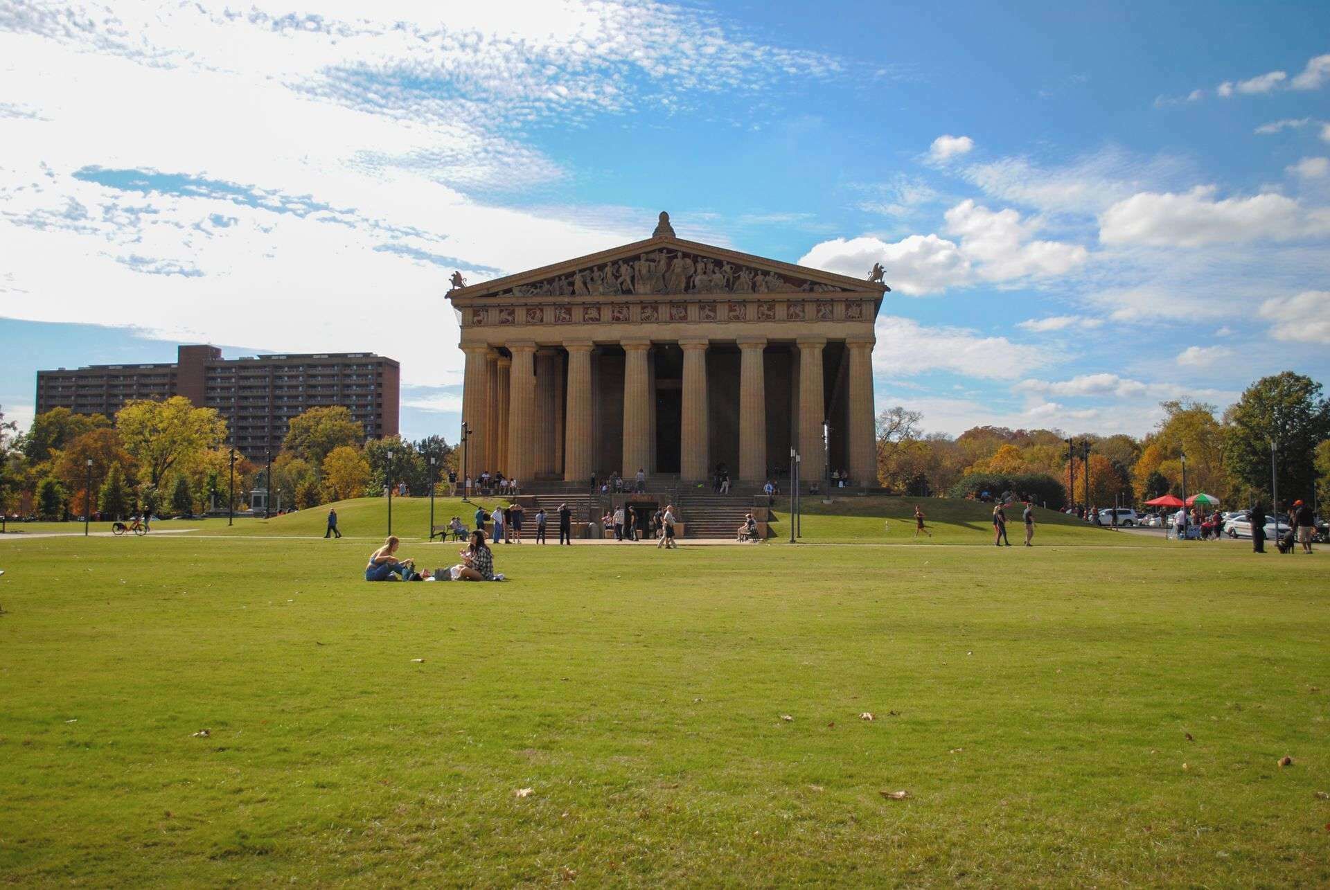 A large open grassy area with a classical building featuring columns and a triangular pediment.