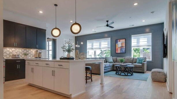 A modern kitchen with dark cabinets, a white island, and pendant lighting. There is a dining area with a sofa and a coffee table. - Roomy 1-Level Condo Near Vanderbilt With Parking    |    1 Story, Secure Parking, Patio. 3 miles to Broadway (Nashville)