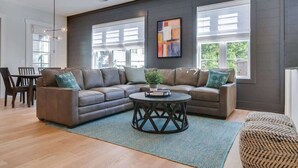 A modern living room with a sectional sofa, a round coffee table, and large windows. - Roomy 1-Level Condo Near Vanderbilt With Parking    |    1 Story, Secure Parking, Patio. 3 miles to Broadway (Nashville)
