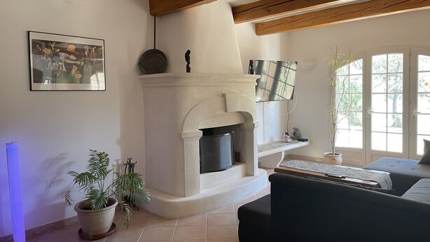 A cozy living room with a fireplace, a television mounted above it, and a large window providing natural light. - Villa in the heart of Provence (Fuveau)