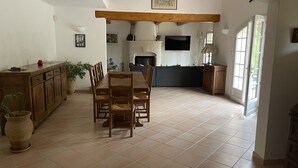 A spacious living area with a wooden dining table and chairs, a fireplace, and a kitchen area with a TV. - Villa in the heart of Provence (Fuveau)