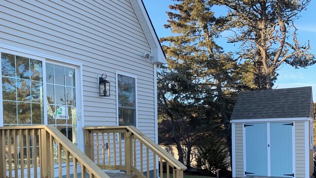 A house with a wooden staircase leading to a deck, a garage, and a large tree in the background. - New construction. Short Walk to Beautiful Ridegevale Beach (Chatham)
