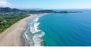 Vista aérea de una playa con costa clara, playa arenosa y vegetación circundante.