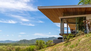 Una casa moderna con techo de madera, amplias ventanas y vistas a colinas verdes.