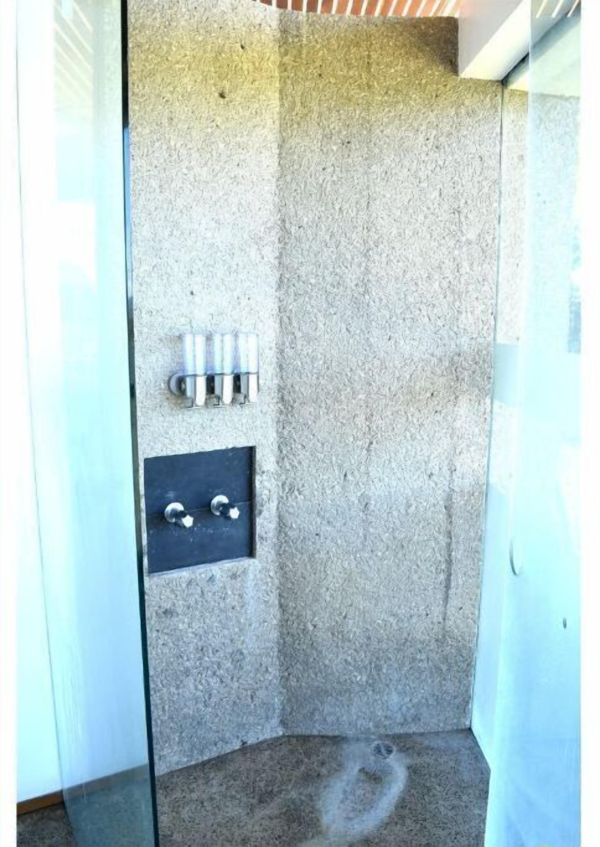 A small, enclosed shower area with a textured wall, a metal panel with a faucet, and a glass door.