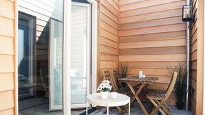 Pieni patio, jossa on pyöreä pöytä ja kaksi tuolia, ruukussa oleva kasvi ja kynttilä.