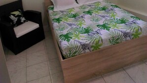 A bedroom with a bed, a nightstand, a chair, and wall decor. - Dépendance Avec Entrée Privée et Terrasse (Fort-de-France)