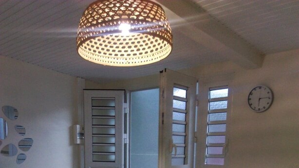 A compact living space with a dining table, chairs, a sofa, a patterned tablecloth, a hanging light fixture, and a clock on the wall. - Dépendance Avec Entrée Privée et Terrasse (Fort-de-France)