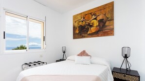 Et soveværelse med seng, et natbord, en lampe, et maleri og et vindue med udsigt.