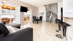 Et moderne opholdsrum med en murstensvæg, et fladskærms-TV, et spiseområde og en spiraltrappe.