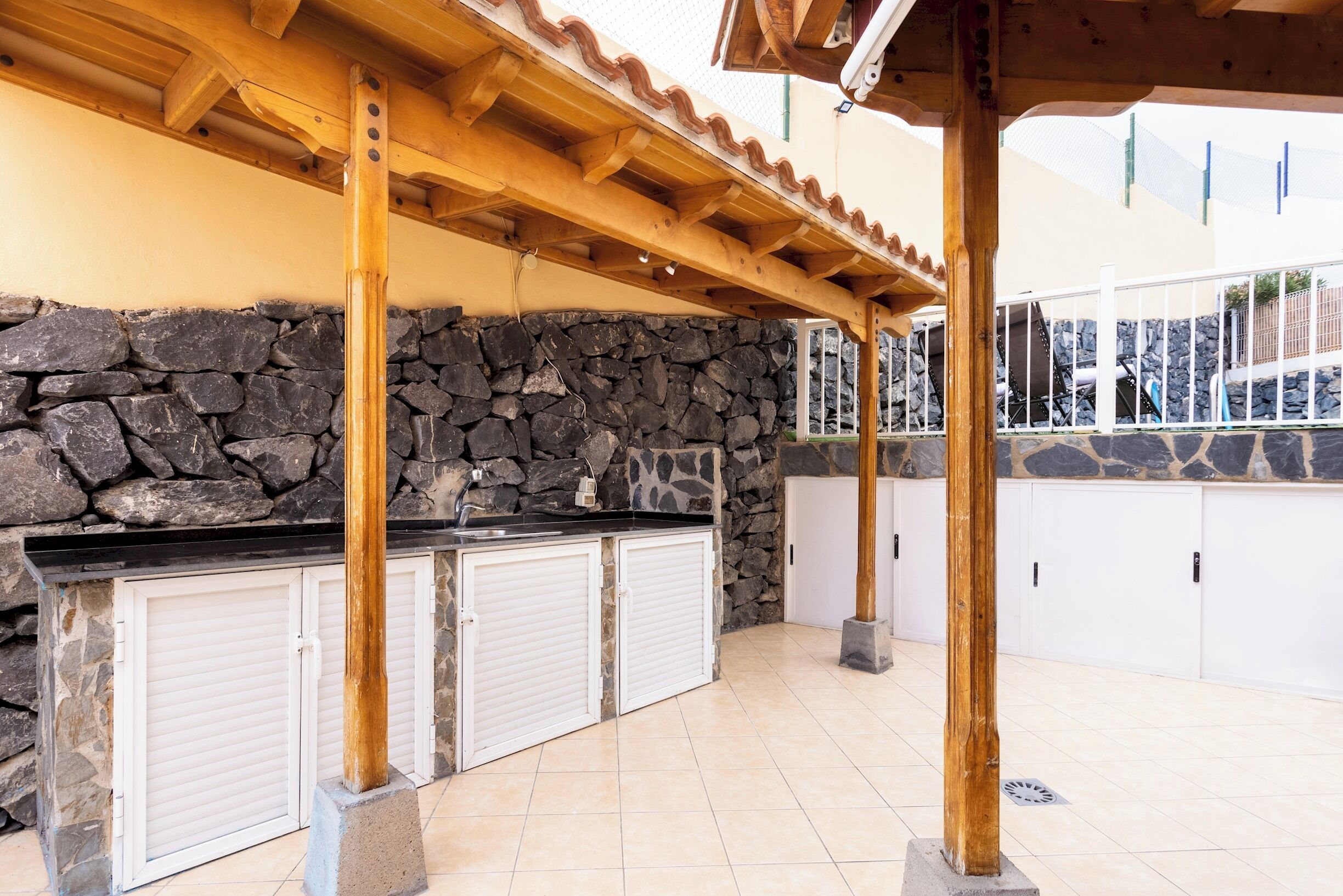 Un espace cuisine extérieur doté de murs en pierre, de poutres en bois et de meubles blancs.