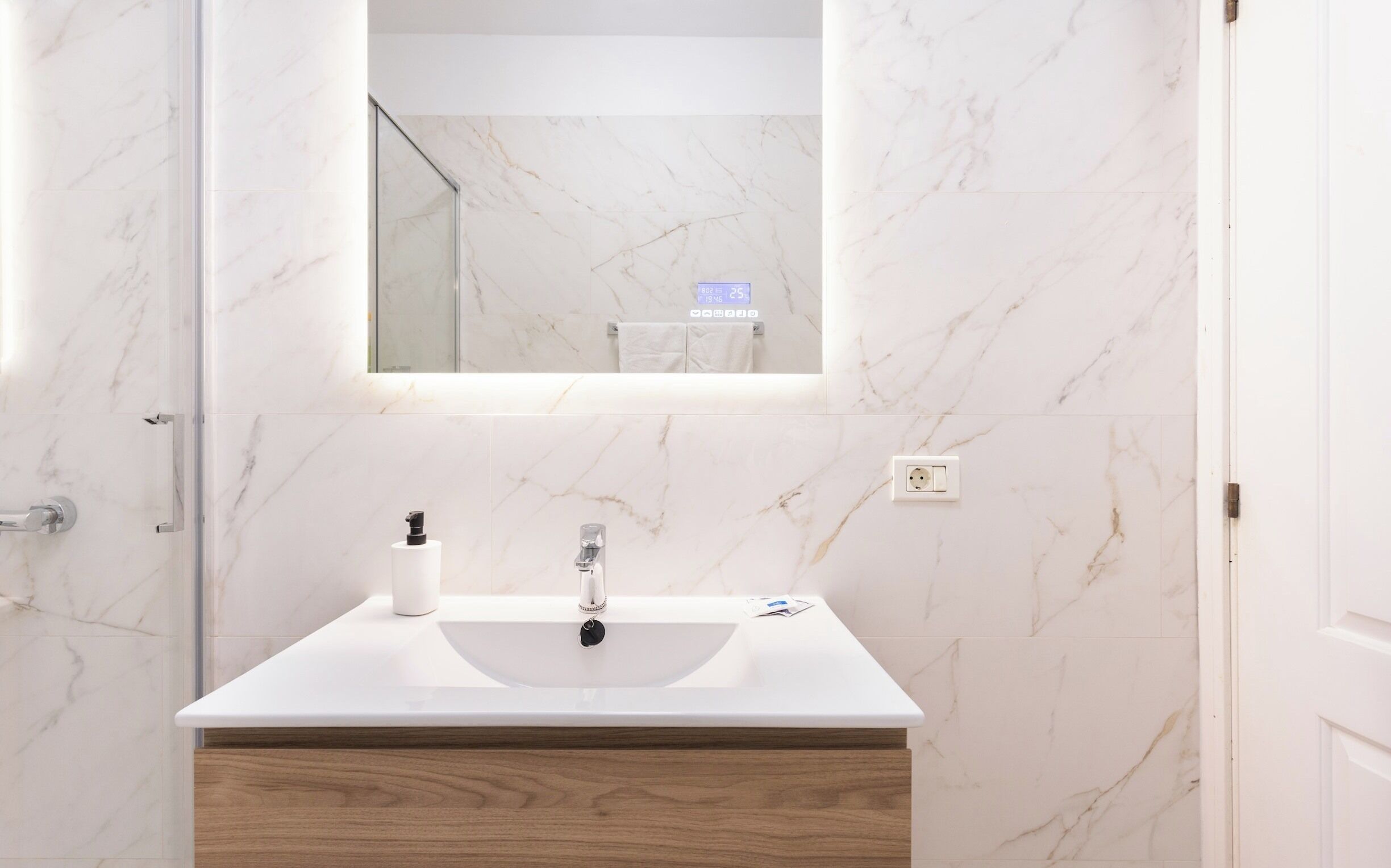 Un bagno con lavabo in marmo bianco, uno specchio e un mobile in legno.