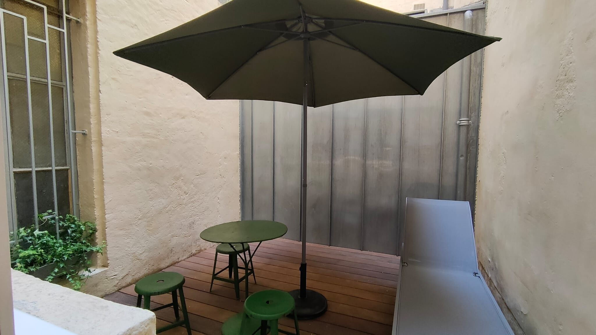 Une petite terrasse extérieure avec une table et deux chaises, un grand parasol et une plateforme en bois.