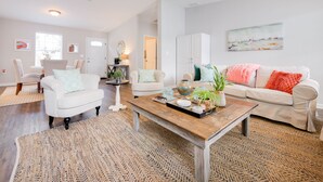 Un salon spacieux avec une table basse en bois, deux canapés blancs, un ventilateur de plafond et une grande fenêtre.