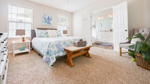 Une chambre à coucher comprenant un lit, des tables de chevet, un ventilateur de plafond et une salle de bain avec un lavabo et un miroir.