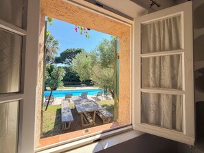 Blick durch ein Fenster auf einen Pool, Gartenmöbel und Grünflächen.