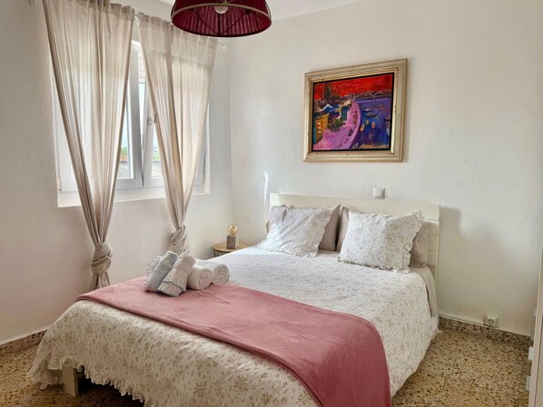Une chambre à coucher avec un lit, des rideaux, un tableau et une table de chevet.