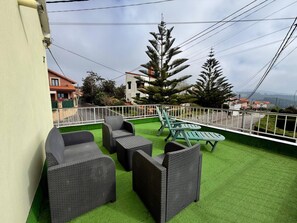 Une terrasse extérieure aménagée avec des meubles en osier et un gazon synthétique, le tout entouré d’une rambarde blanche.