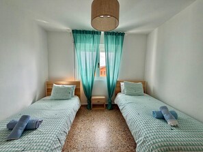 A room with two beds, a wooden headboard, a small bedside table, and a window with curtains. - Apartment in Ajo - Antuerta 12006 (Cantabria)