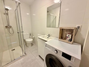 Une salle de bain moderne avec une douche à parois de verre, des toilettes, un lave-linge et un lavabo.