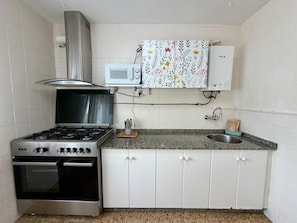 Une cuisine compacte équipée d’une cuisinière à gaz, d’un four, d’un four à micro-ondes et d’un petit évier.