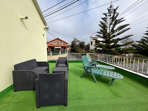 An outdoor seating area with wicker furniture and artificial grass, surrounded by a white fence and a large tree. - Apartment in Ajo - Antuerta 12006 (Cantabria)