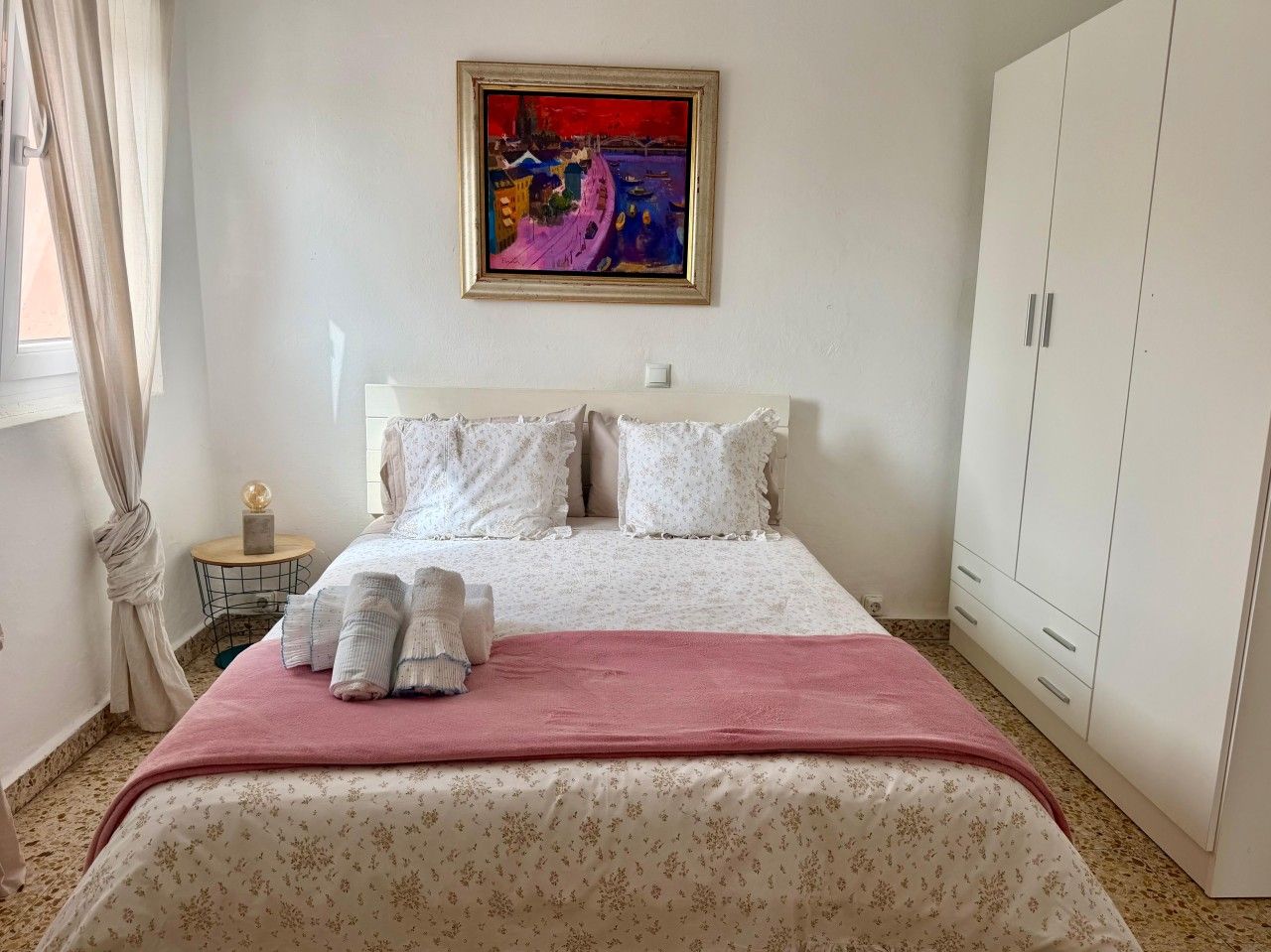 Une chambre d’hôtel avec un lit, une armoire, un tableau au mur et une fenêtre avec des rideaux.