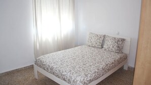 Un lit simple avec une couvre-lit à motifs, dans une pièce aux murs blancs et au plancher en bois.