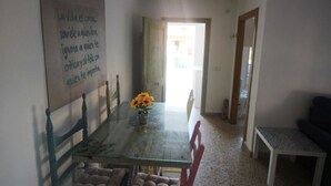 Un coin repas avec une table en verre, des chaises et un vase rempli de fleurs. Une porte donne accès à une autre pièce.