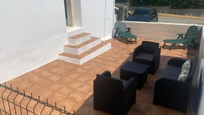 Ein Balkon mit Gartenmöbeln, eine Treppe und der Blick auf einen parkenden Wagen und Gebäude.