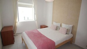 Ein Schlafzimmer mit Bett, Nachttisch, Holzschrank und einem Fenster mit Vorhängen.