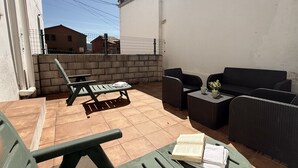 A patio with outdoor furniture, a tiled floor, and a white wall.